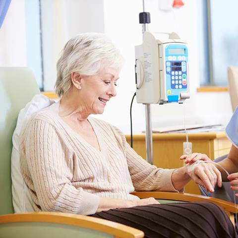 Stock image of a woman sitting in a chair with a drip in her left hand which is being checked by a person in medical scrubs